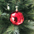 A red, round, shiny Christmas ornament hanging on a Christmas tree with green needles.